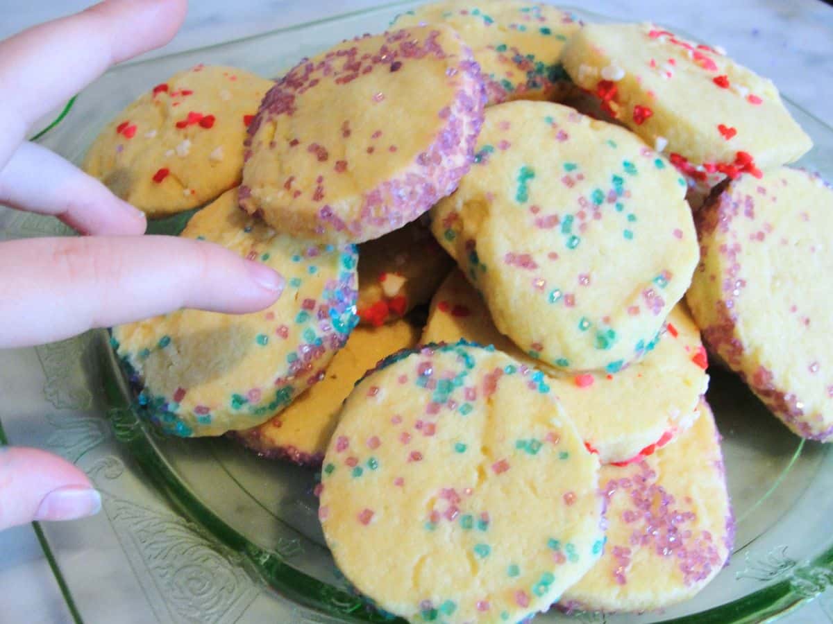 child's hand picking up a sprinkle covered spring sugar cookie off a pile of cookies