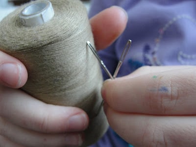 person holding spool or brown thread and embroidery needles in hand