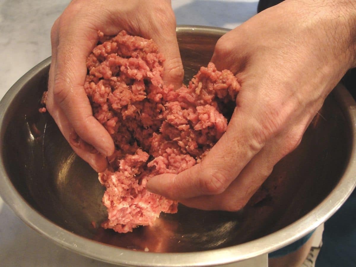 raw ground beef with hands in bowl making beef burger patties