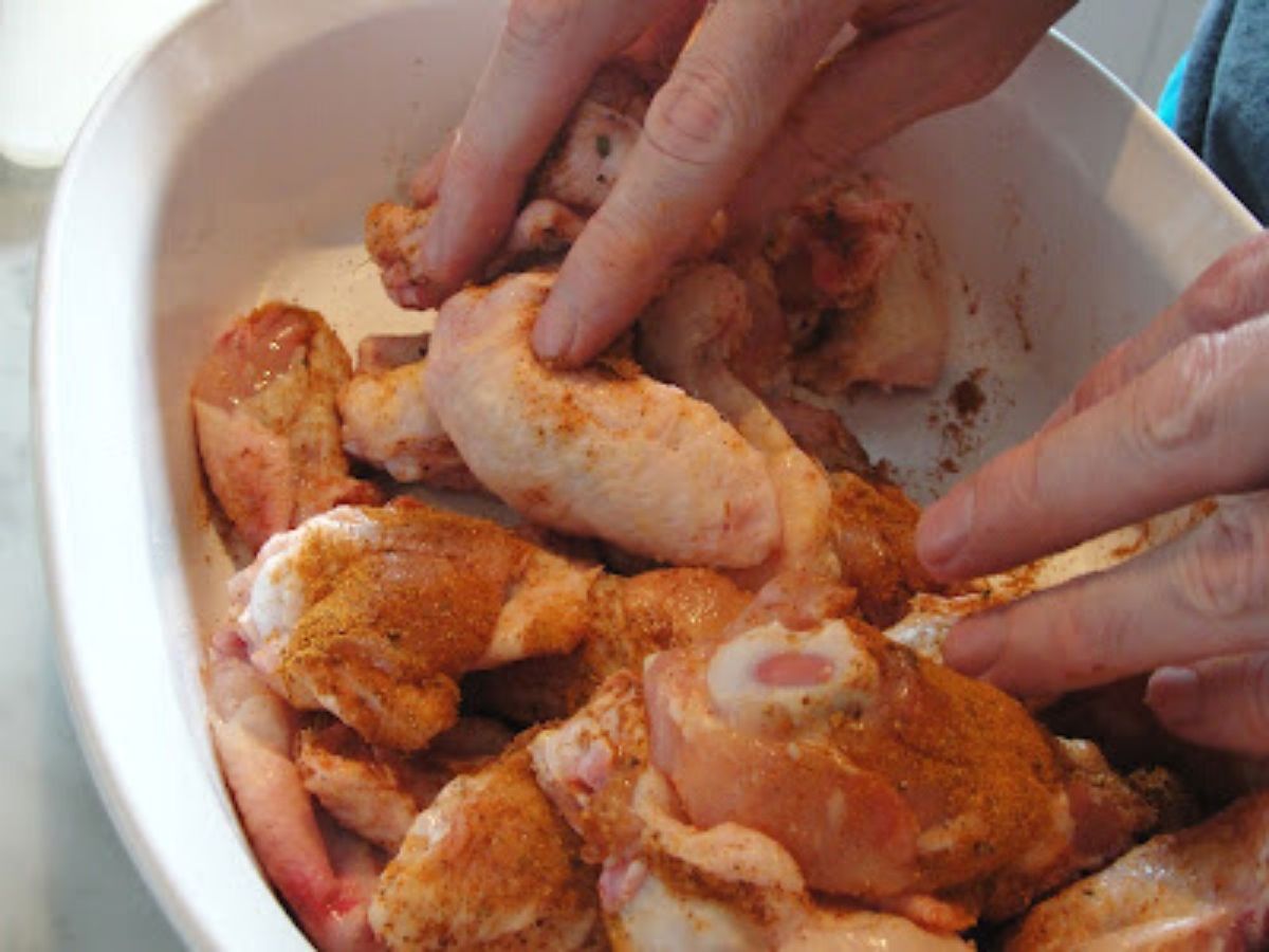 chicken wings with spice rub being rubbed on with hands