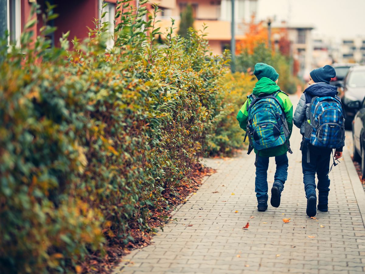 two kids walking on sidewalk with backpacks on