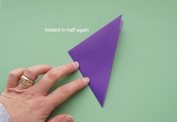 origami paper folded in half again for paper snowflake, being pressed by woman's fingers