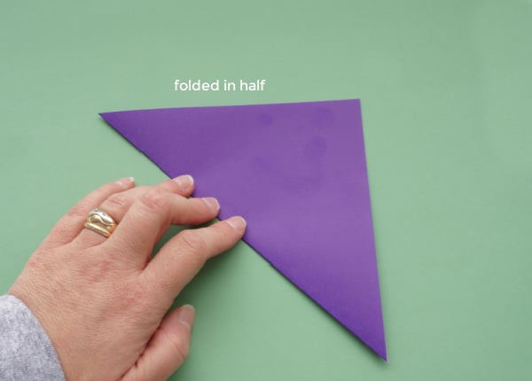 origami paper folded in half for paper snowflake, with woman's hand