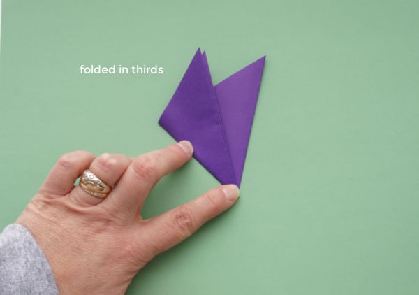 origami paper snowflake folded in thirds with fingers pressing on the fold
