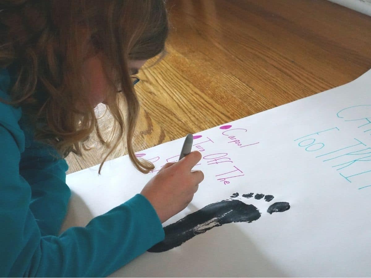 kid writing ways to reduce your carbon footprint on poster