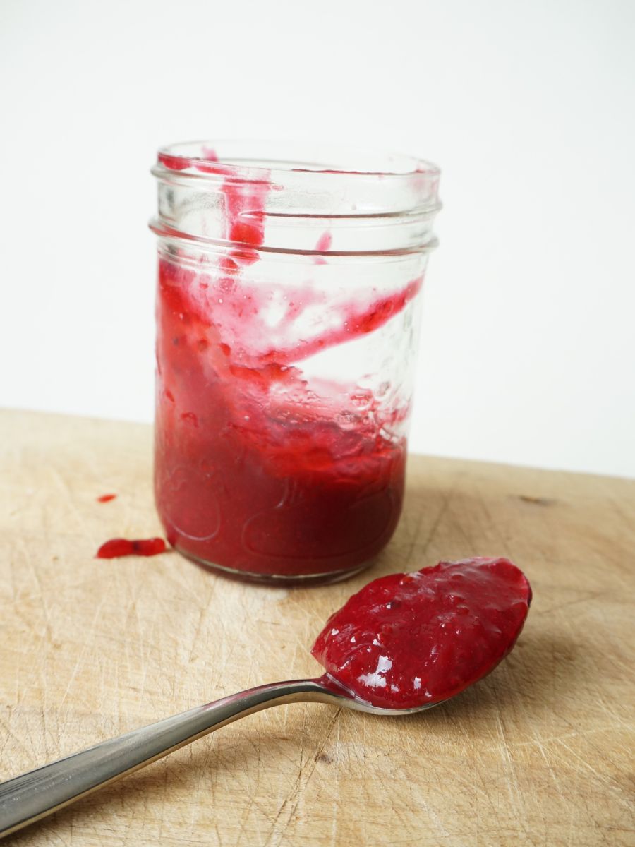 mason jar of homemade red currant sauce and spoon filled with sauce