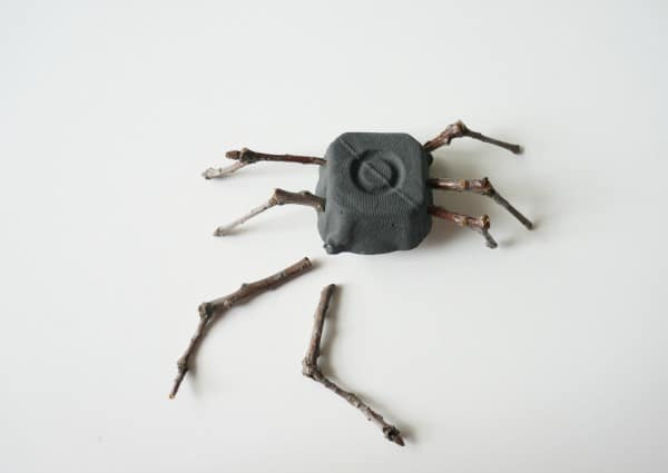 egg carton spider with twig legs being poked into the egg carton