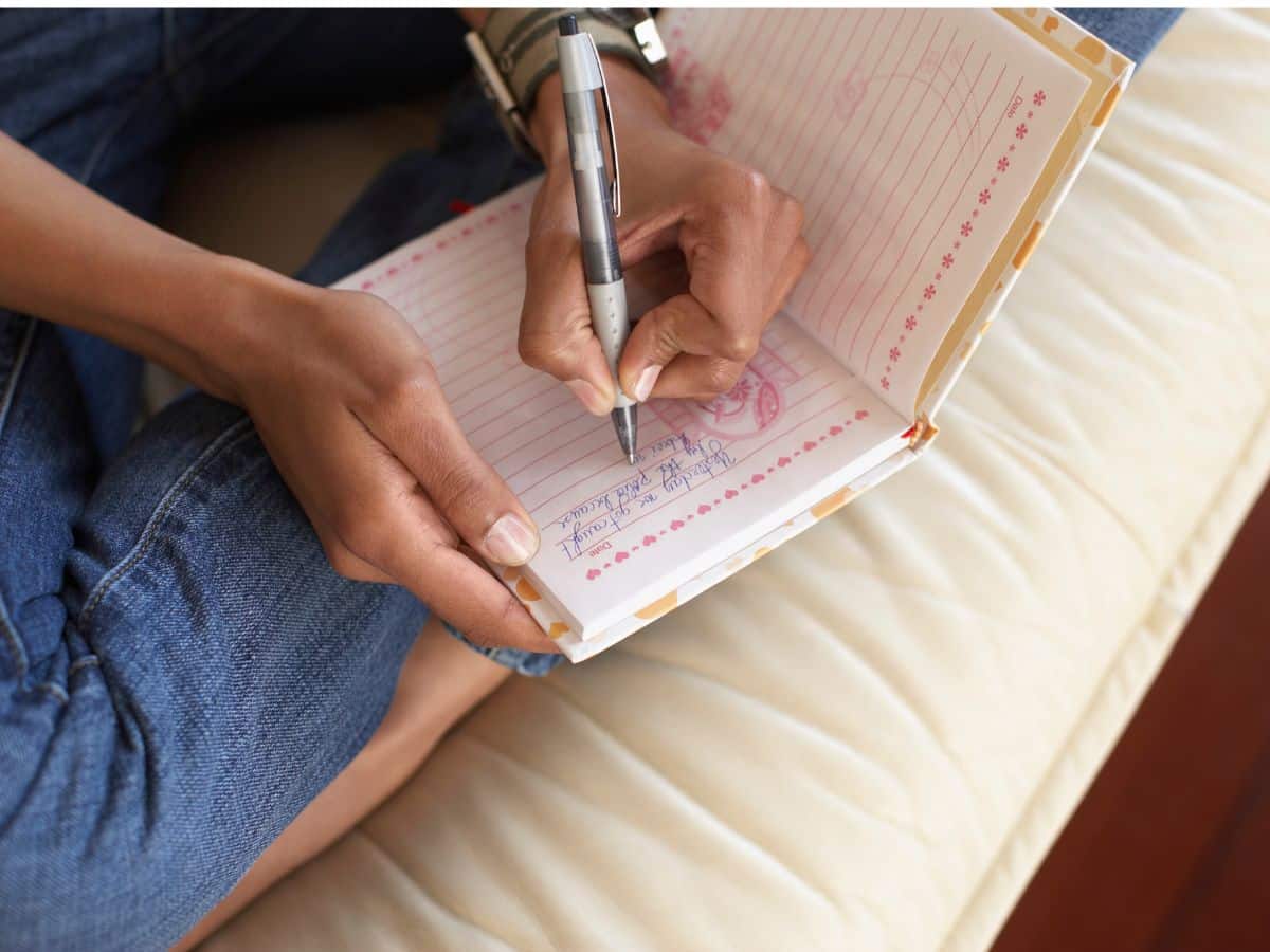 tween writing in journal while sitting on bed