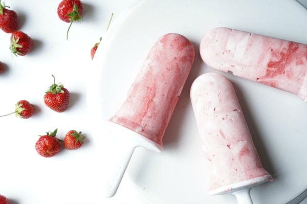 strawberries around strawberry creamsicle popsicles on a white plate