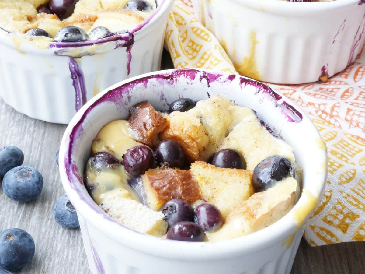 close up of easy blueberry bread pudding in ramekin with blueberries around it