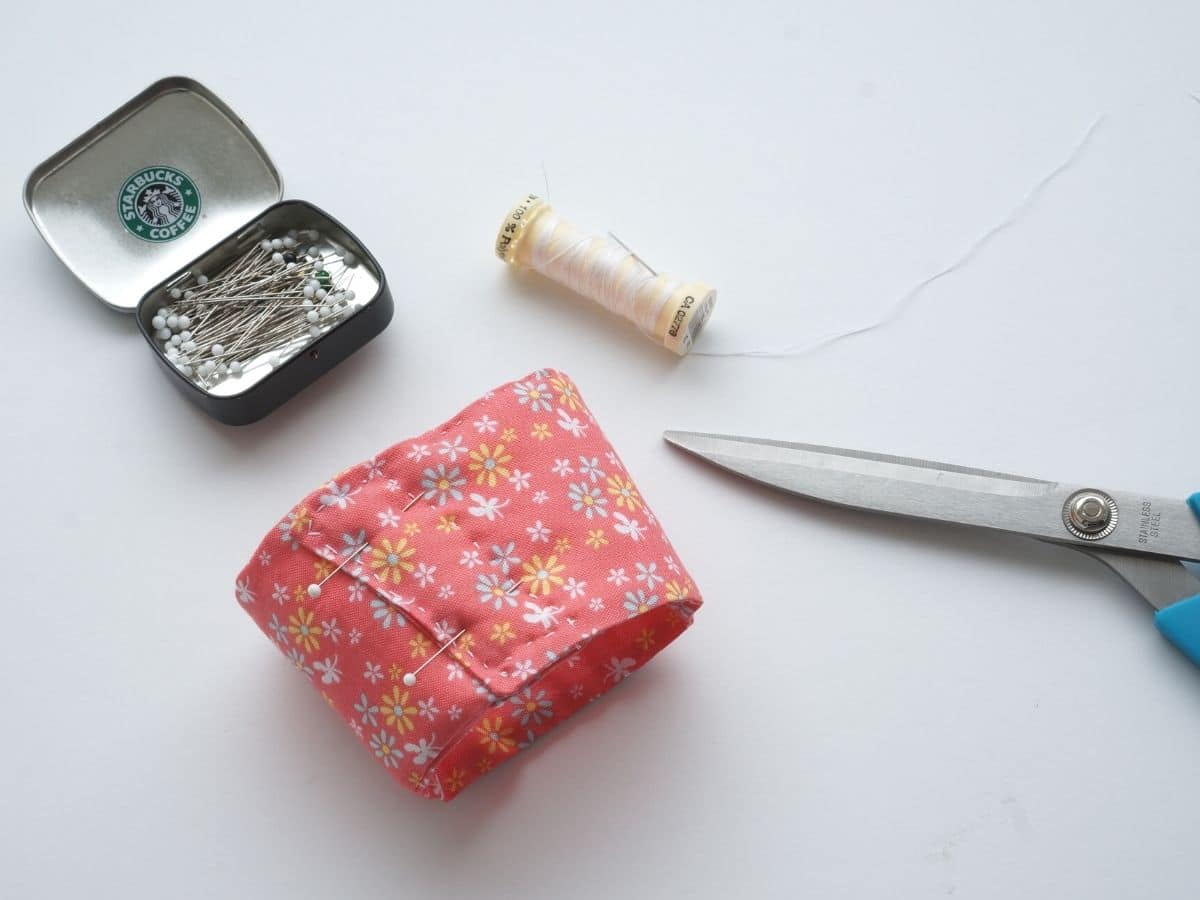 cotton coffee sleeve wrapped around and pinned in a cylinder shape with thread and scissors and dish of pins