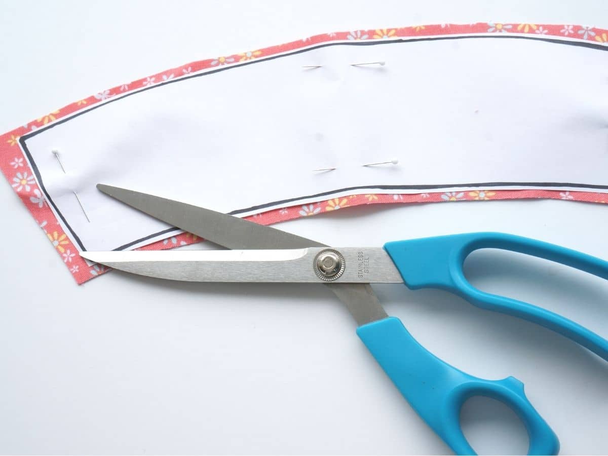 coffee sleeve paper template pinned onto flowery cotton fabric cut out with pair of blue handled scissors
