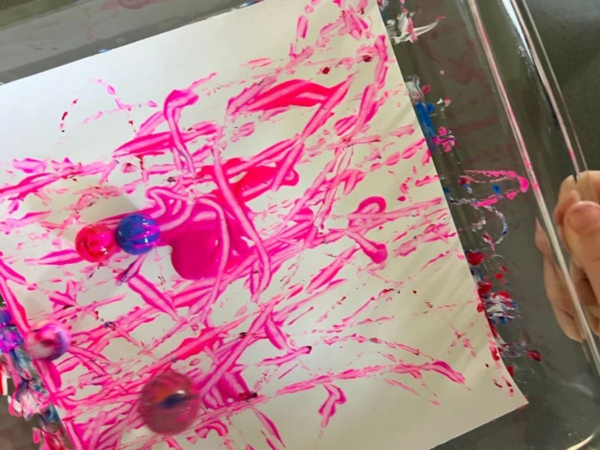 painting with marbles on paper inside a baking dish