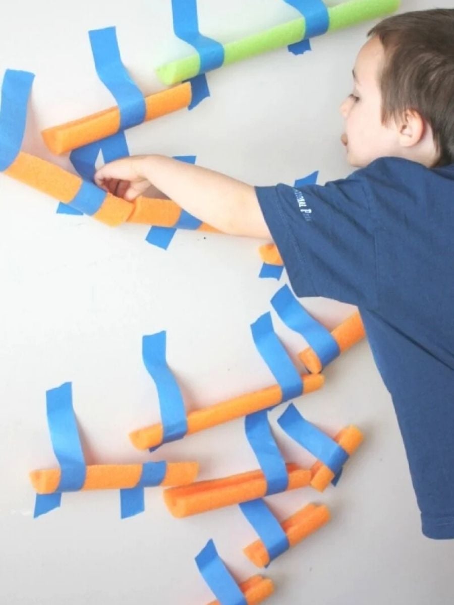 pool noodle marble run taped to the wall with a kid