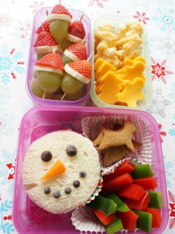 close up of christmas lunch box filled with christmas-theme lunch - snowman sandwich, grinch grapes and gingerbread cheese slices