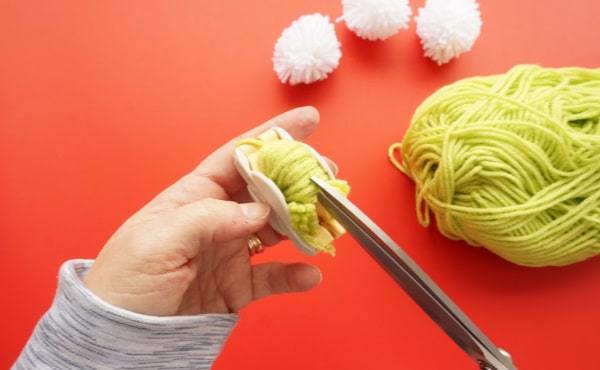 pom pom maker with scissors cutting around the pompom maker