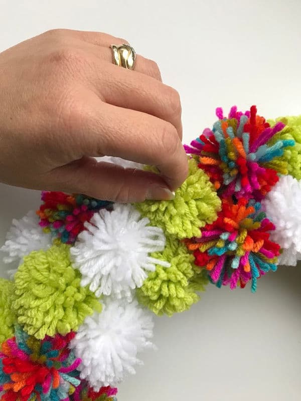 pom poms being glued onto a wreath form with a hand