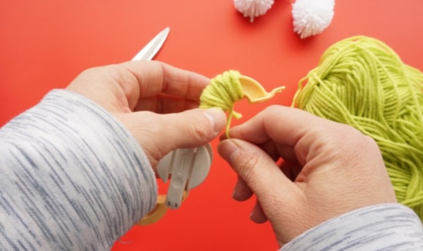 yarn wrapped around a pom pom maker with hands