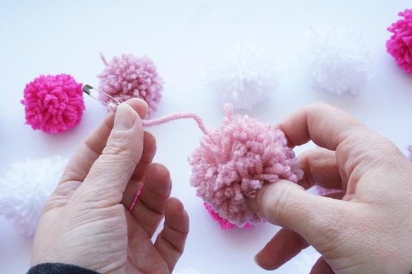 feed the pom pom with safety pin onto yarn garland