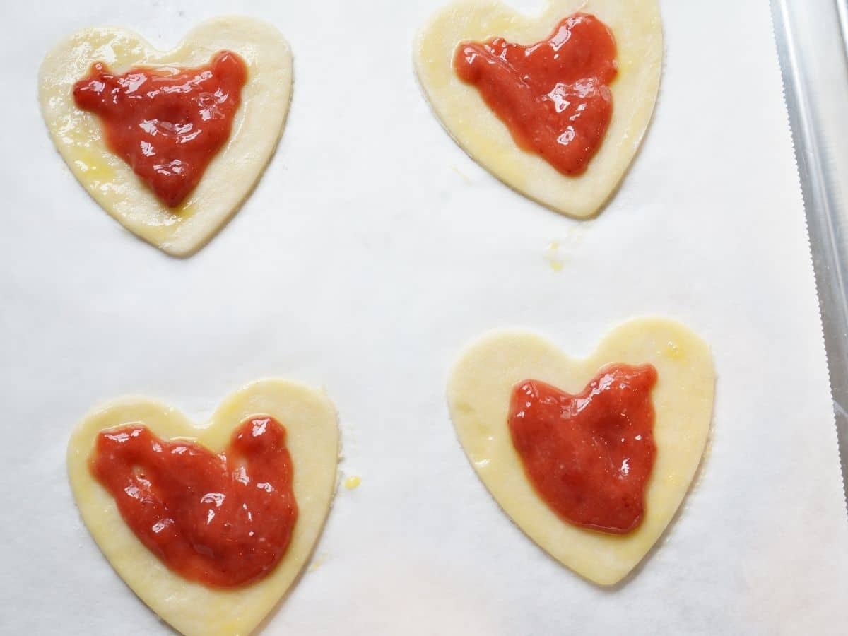 pastry hearts with strawberry jam filling on baking sheet