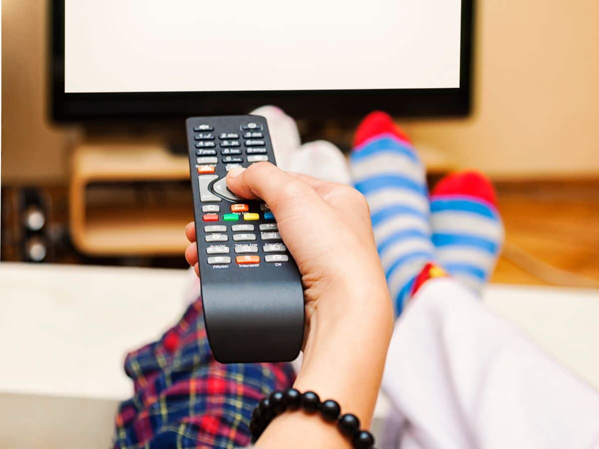 tween hand holding tv remote pointing at tv screen with feet in the background