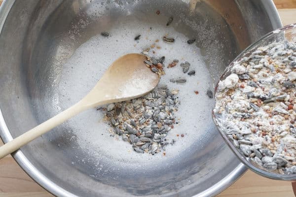 bird seed going into metal bowl with gelatin and a wooden spoon