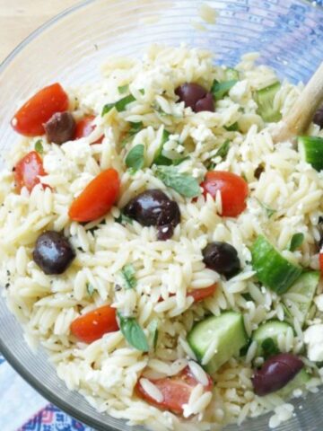 glass bowl filled with Greek pasta salad with orzo pasta, tomatoes, cucumber, basil and olives