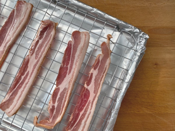 uncooked bacon on baking sheet