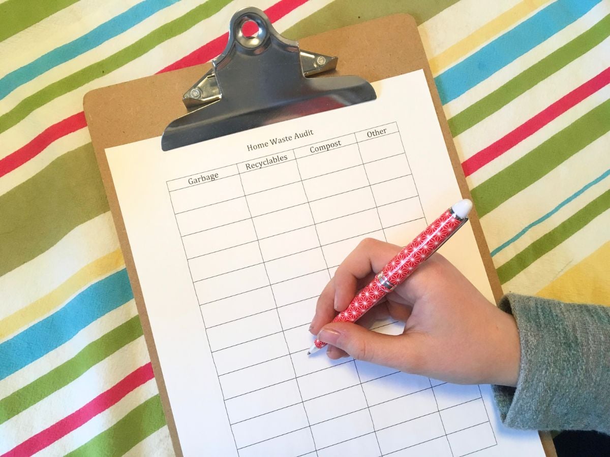 child's hand holding a pen and writing in a home waste audit chart on a clipboard