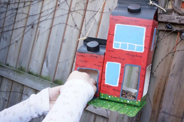 milk carton bird feeder being filled with seed and hanging from tree with child's hand