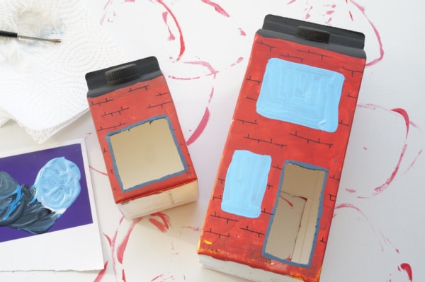 2 milk cartons painted with windows and bricks and black rooftops for bird feeder
