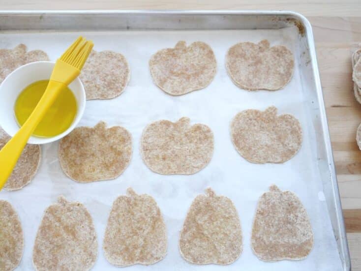 pumpkin shaped tortillas on baking sheet with dish of olive oil and brush