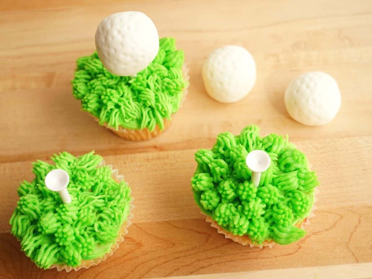 2 golf tee cupcakes with grassy butterbream and fondant golf balls stuffed with mini peanut butter cups on the tee
