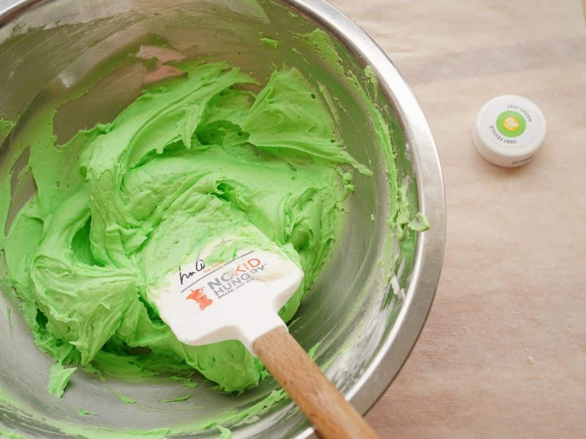 bowl of green buttercream frosting with spatula and green lid from food coloring