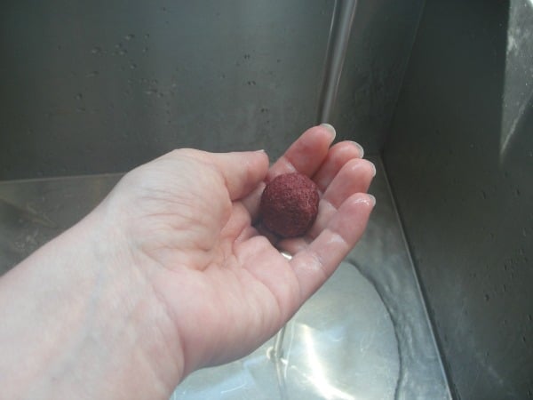 ball of wool roving turning into felt ball in hand with running tap water