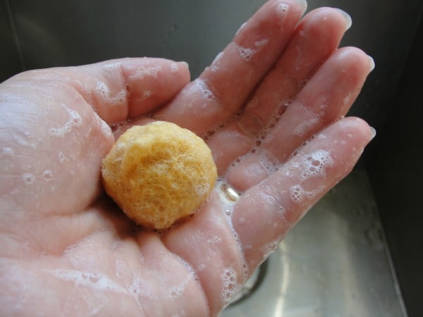 ball of yellow wool roving in soapy hand with running water in sink