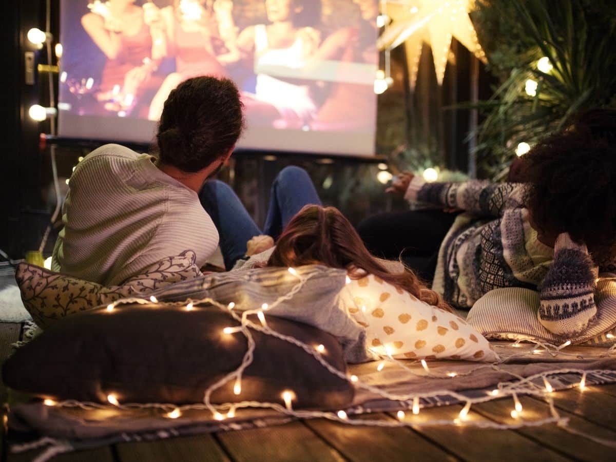 mom dad and kid watching a summer movie in the backyard with twinkle lights