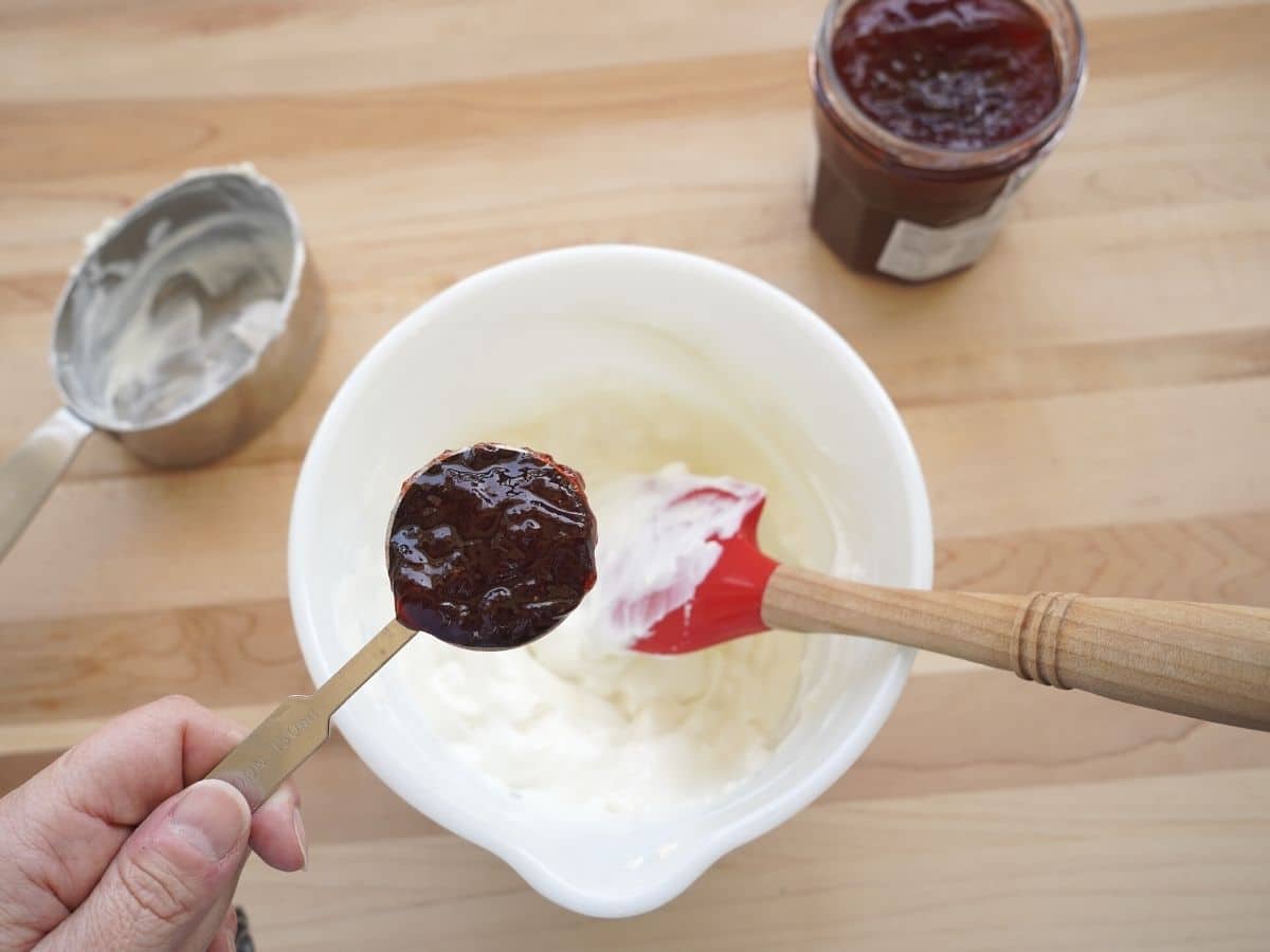 yogurt and cream cheese combined in small bowl with tablespoon of strawberry jam being added