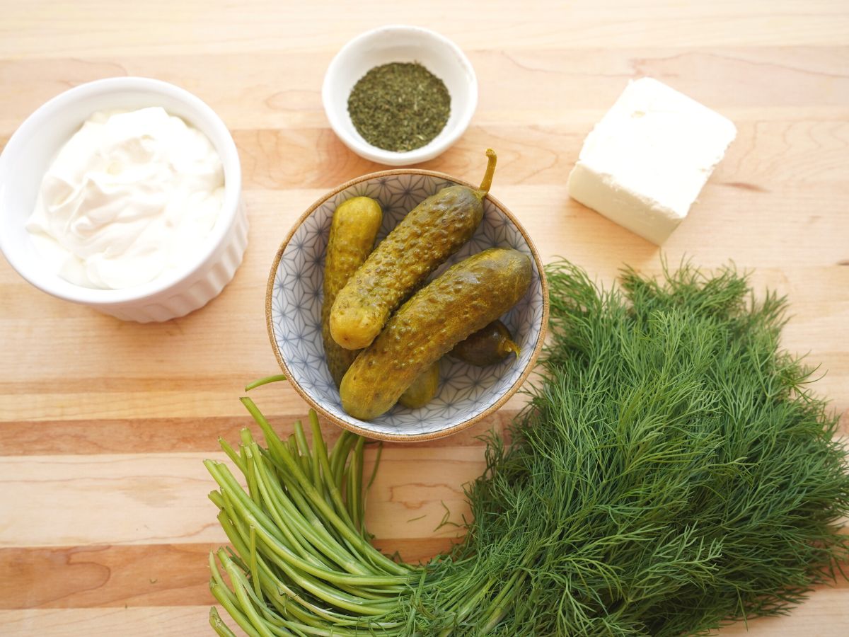 dill pickle dip ingredients on cutting board dill pickles cream cheese sour cream and fresh dill