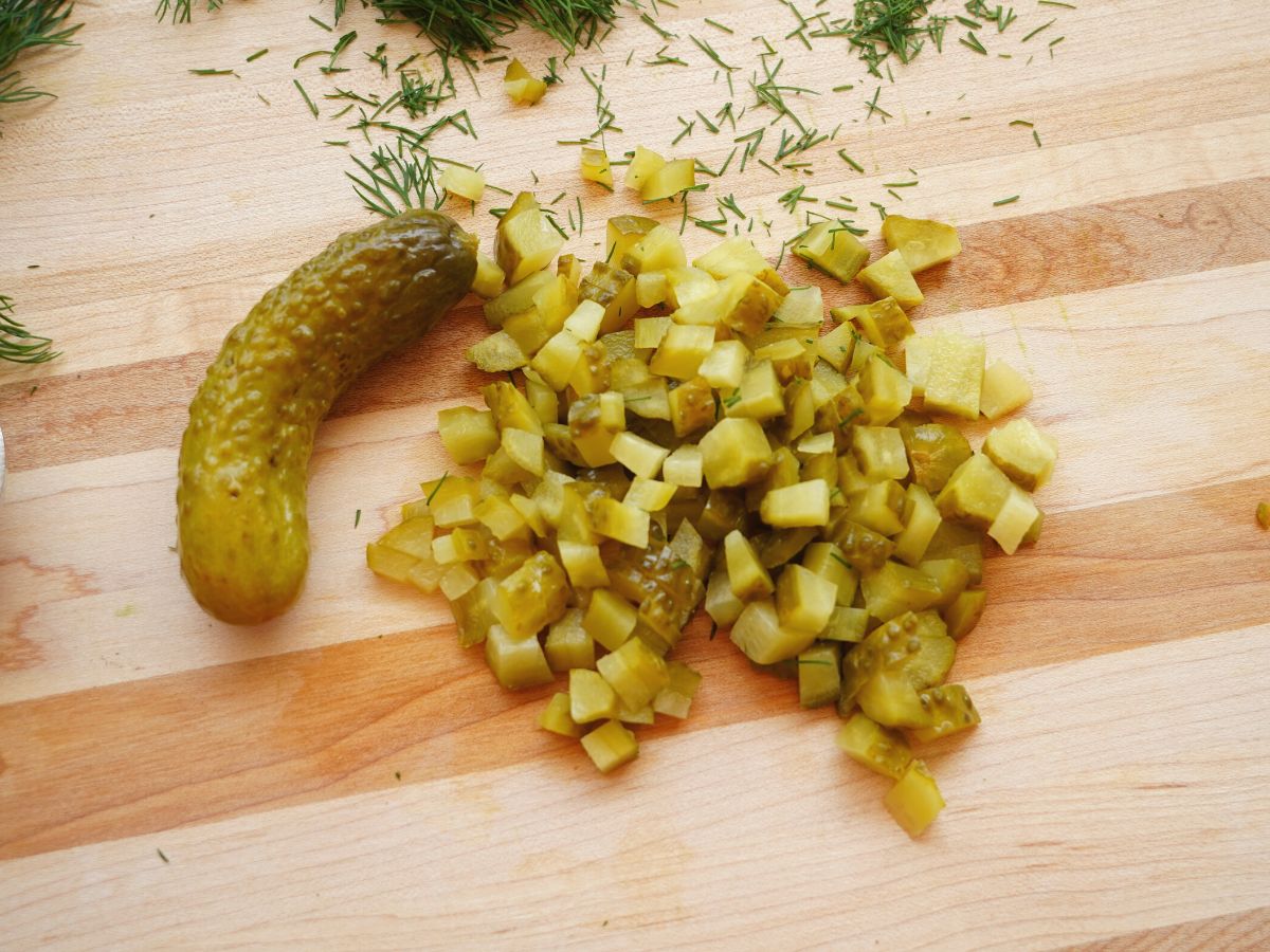 pile of chopped dill pickle on cutting board with chopped fresh dill too