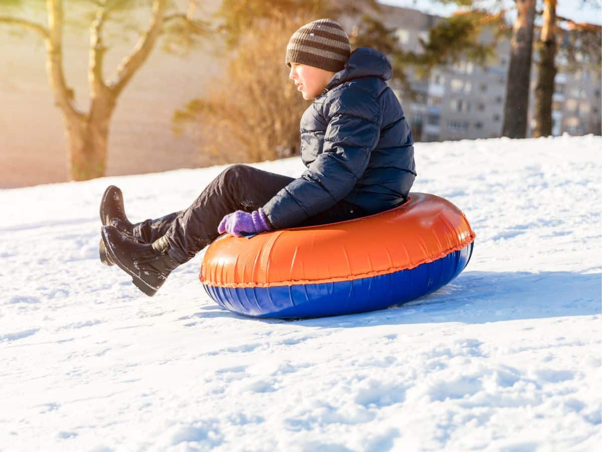tween boy sliding down snowy hill on inner tube