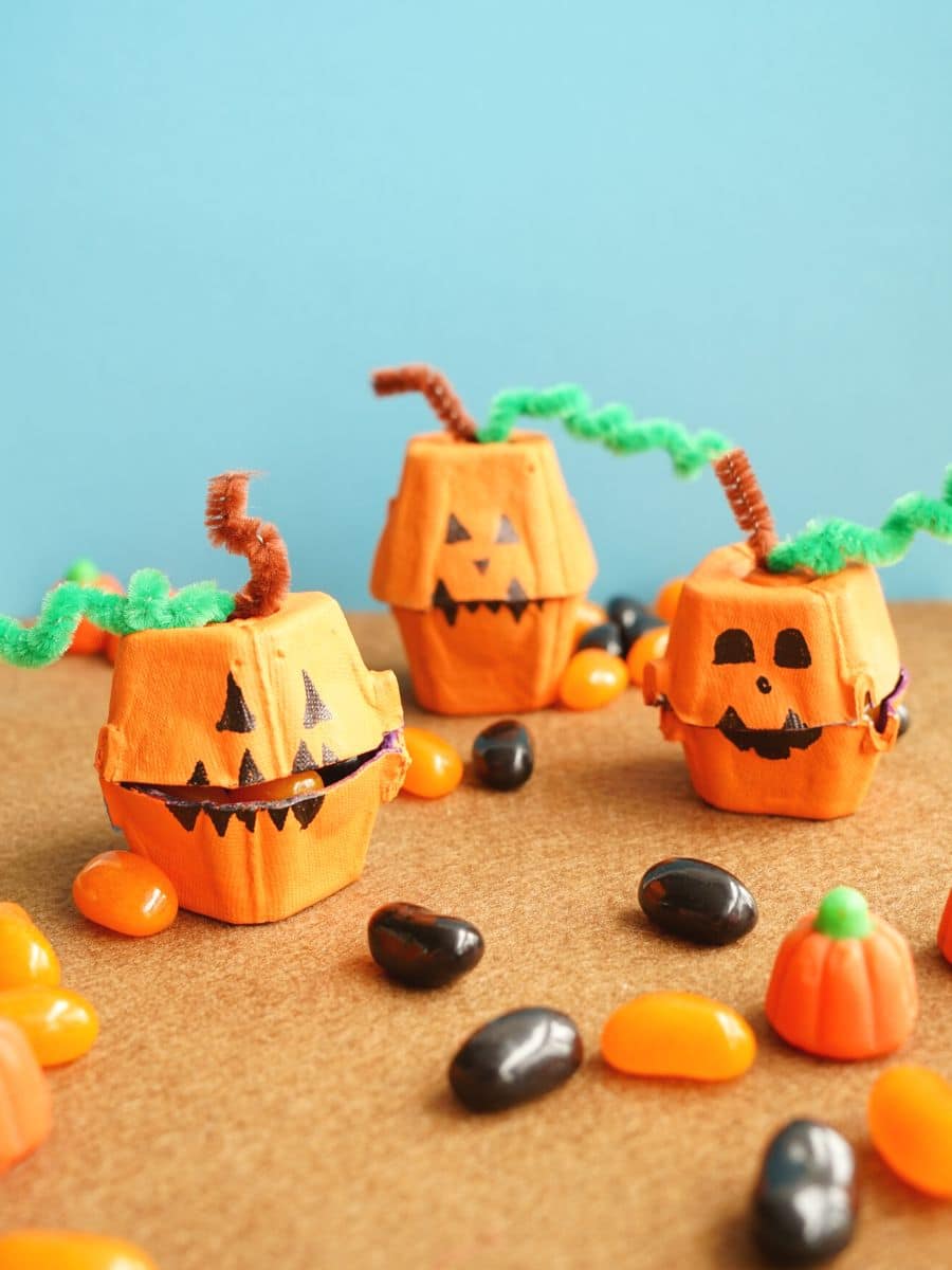 3 egg carton jack o lantern treat boxes filled with candy and surrounded by Halloween candy