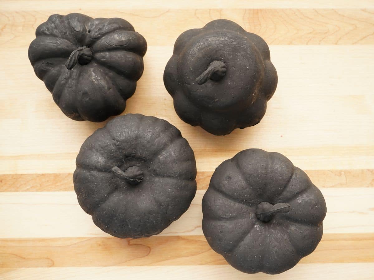 4 little black painted pumpkins sitting on butcher block background