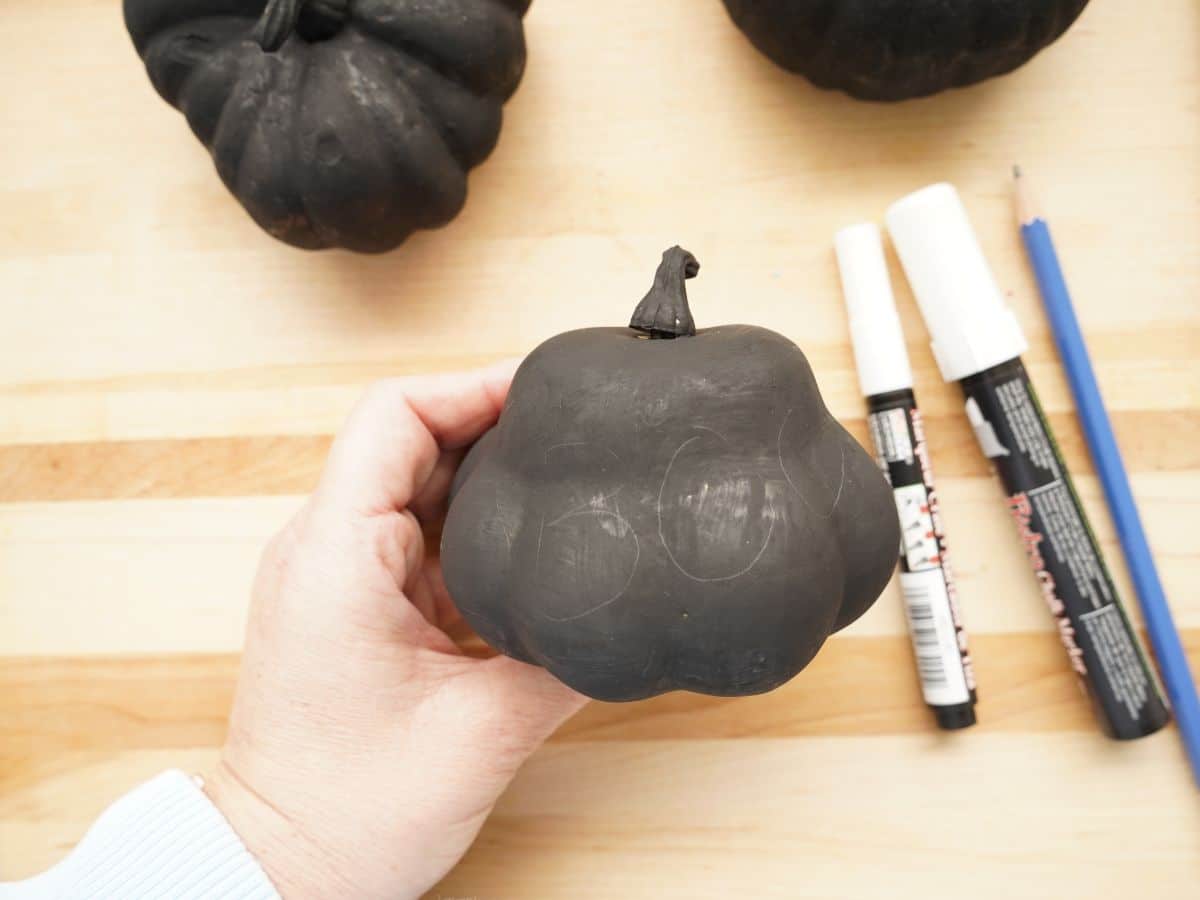 black pumpkin with the word boo drawn on with pencil in woman's hand