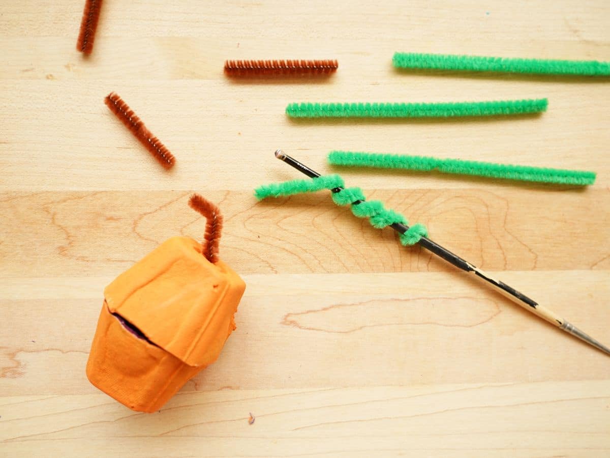 brown pipe cleaner stem in top of egg carton pumpkin and green pipe cleaner wrapped around paintbrush handle