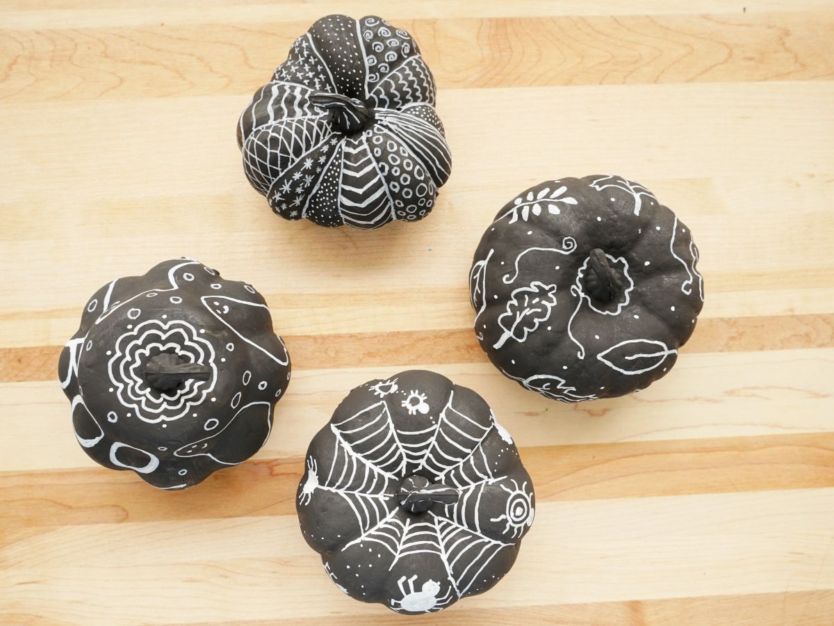 spiders drawn on black pumpkin with chalk marker, ghosts drawn on black pumpkin with chalk marker, leaves drawn on black pumpkin with chalk marker and doodle designs with chalk marker on pumpkins
