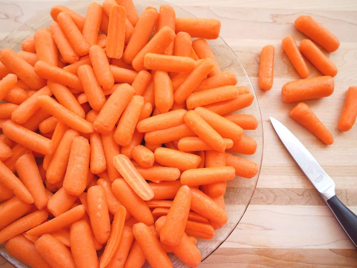 baby carrots sliced and stacked on round glass tray with knife on the side
