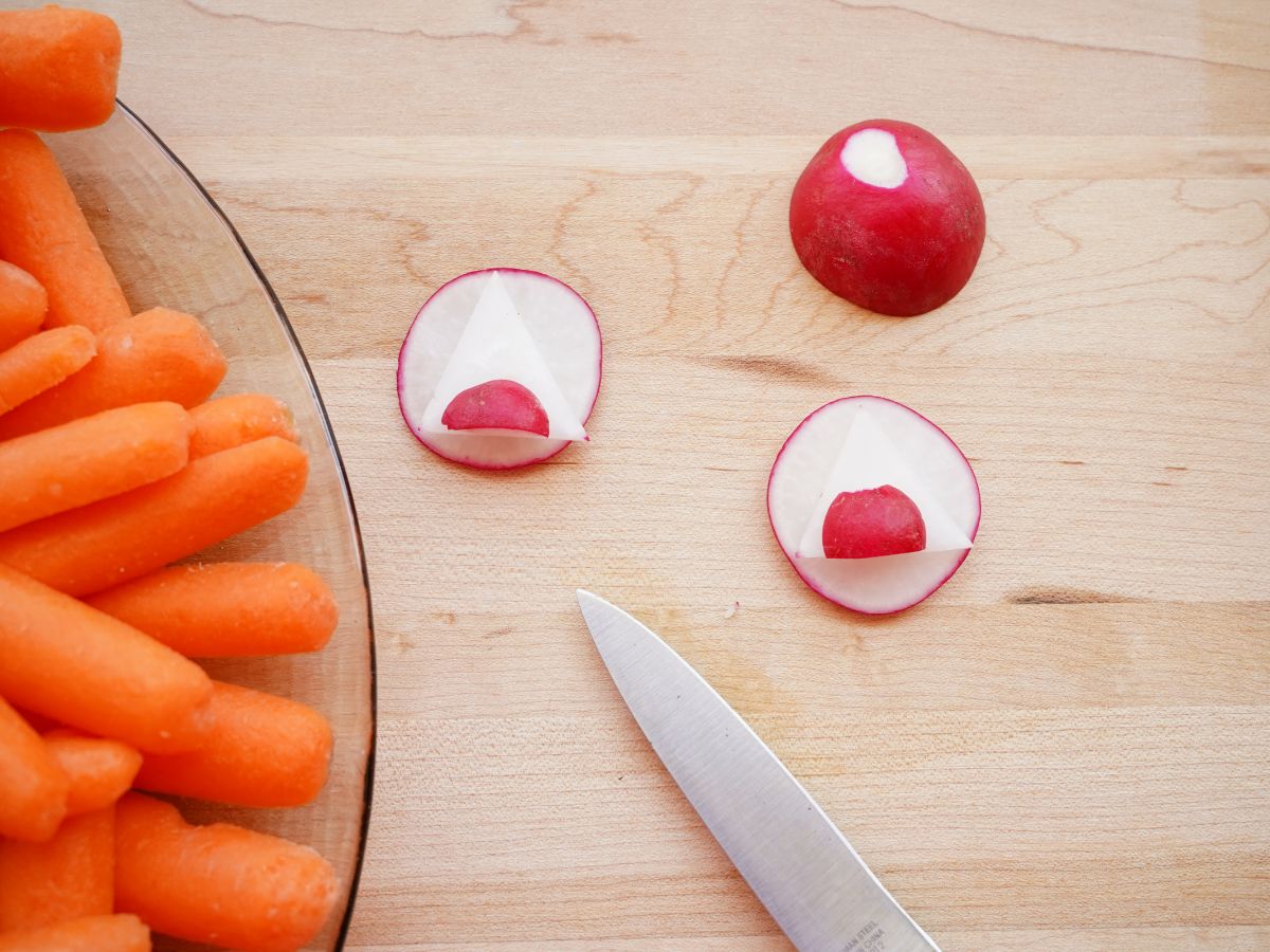 baby carrots on serving tray with radishes sliced into eye shapes and a knife