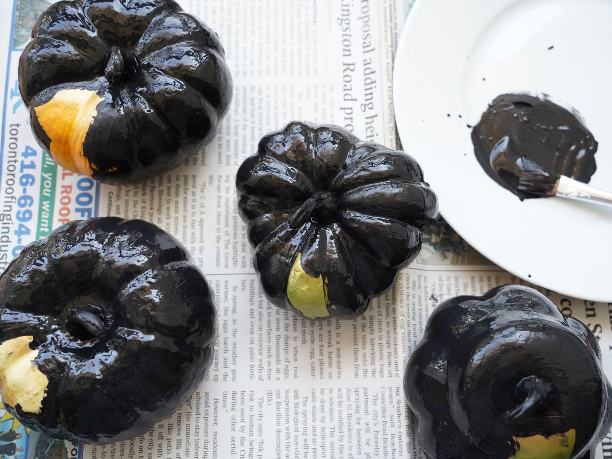 foam pumpkins and gourds painted with black acrylic paint on newspaper background
