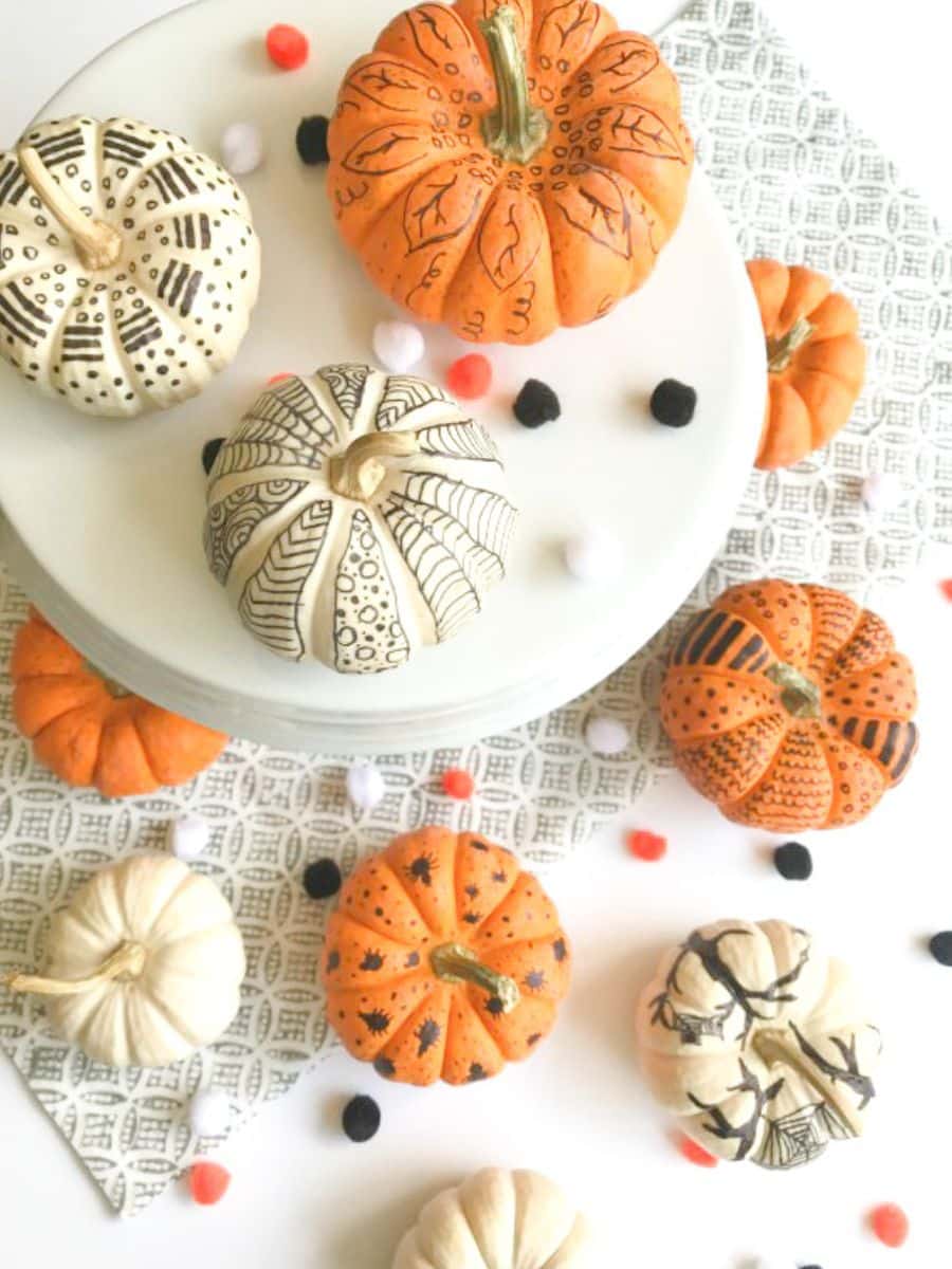 a variety of pumpkins decorated with markers on a table top